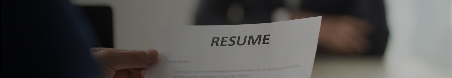 A hand holding a resume. A buisiness person out of focus in the background.