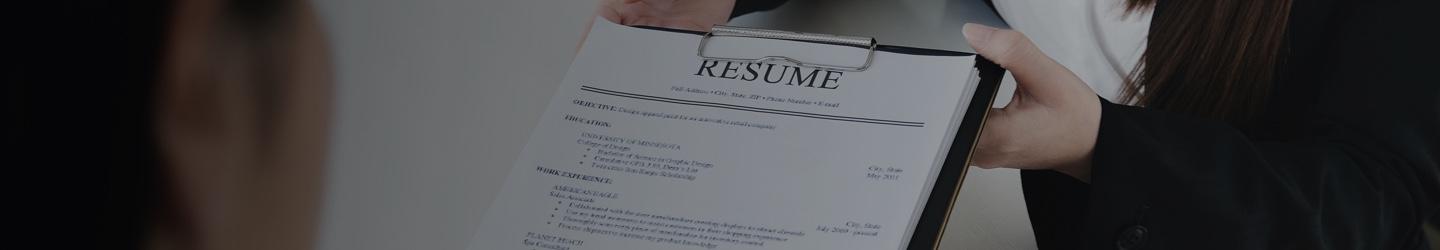 Woman handing over her resume on a clipboard to another businesswoman