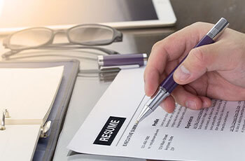 Hand of a man with a pen revising a printed resume at a desk.