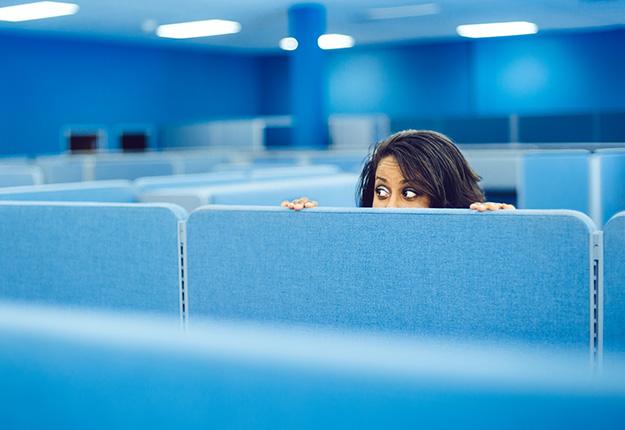 Female worker hiding behind cubicle wall