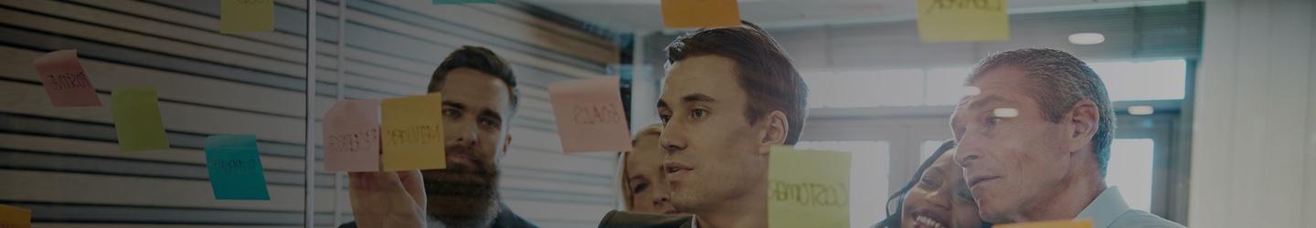 A businessman sticking sticky notes on a glass wall while his colleagues observe