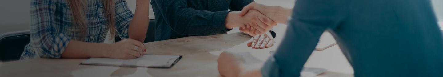 A couple of hiring managers greet a candidate at a table. Two men shake hands.