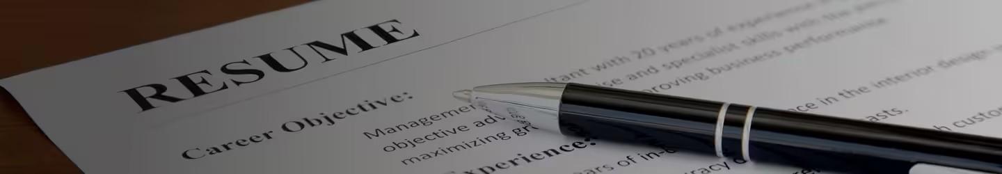 A resume laying on a table with a pen over it.