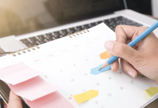 Female hand writing on a sticky note stuck on a calendar