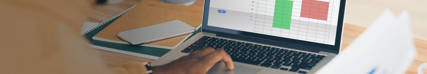 Man on a laptop using a spreadsheet and holding a paper