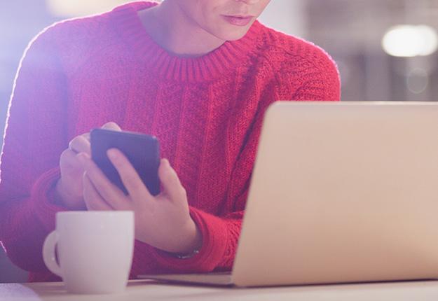 Woman using smartphone while looking at computer