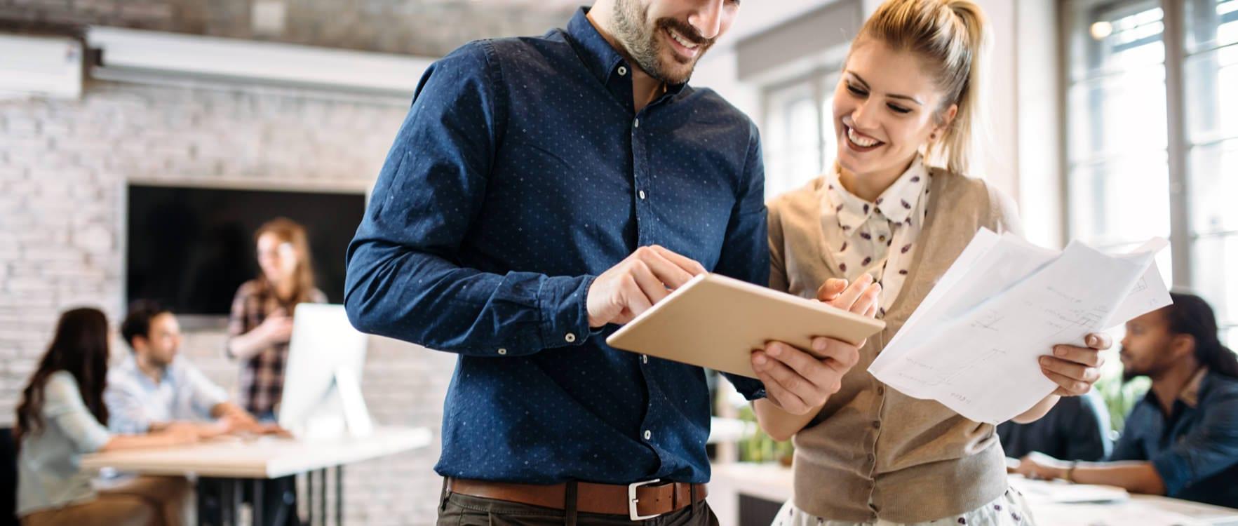 Man a woman in an office look at a tablet while smiling