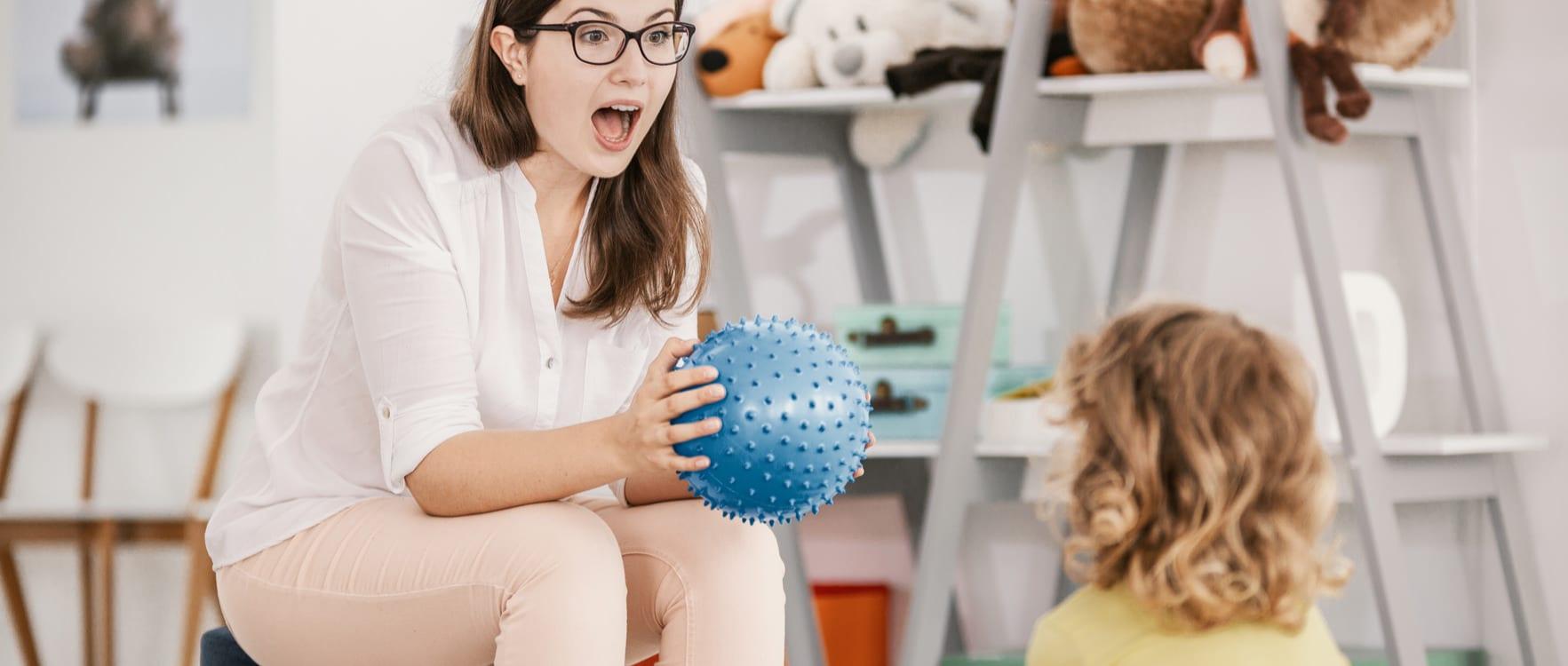 Female therapist holding a therapy ball and talking to a child