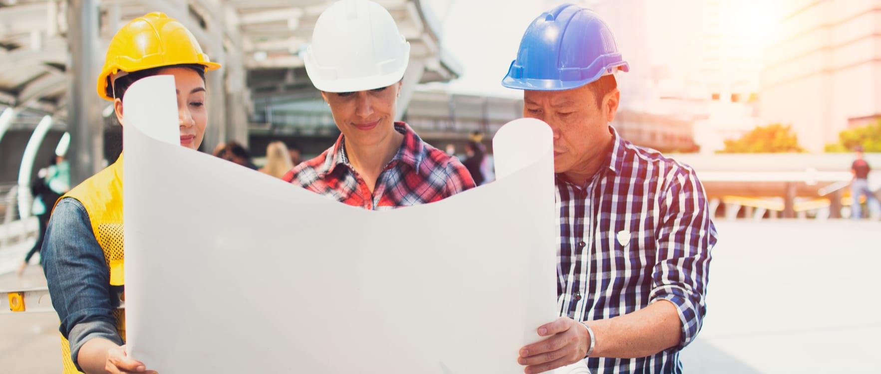 Three people with hard hats looking at construction drawings