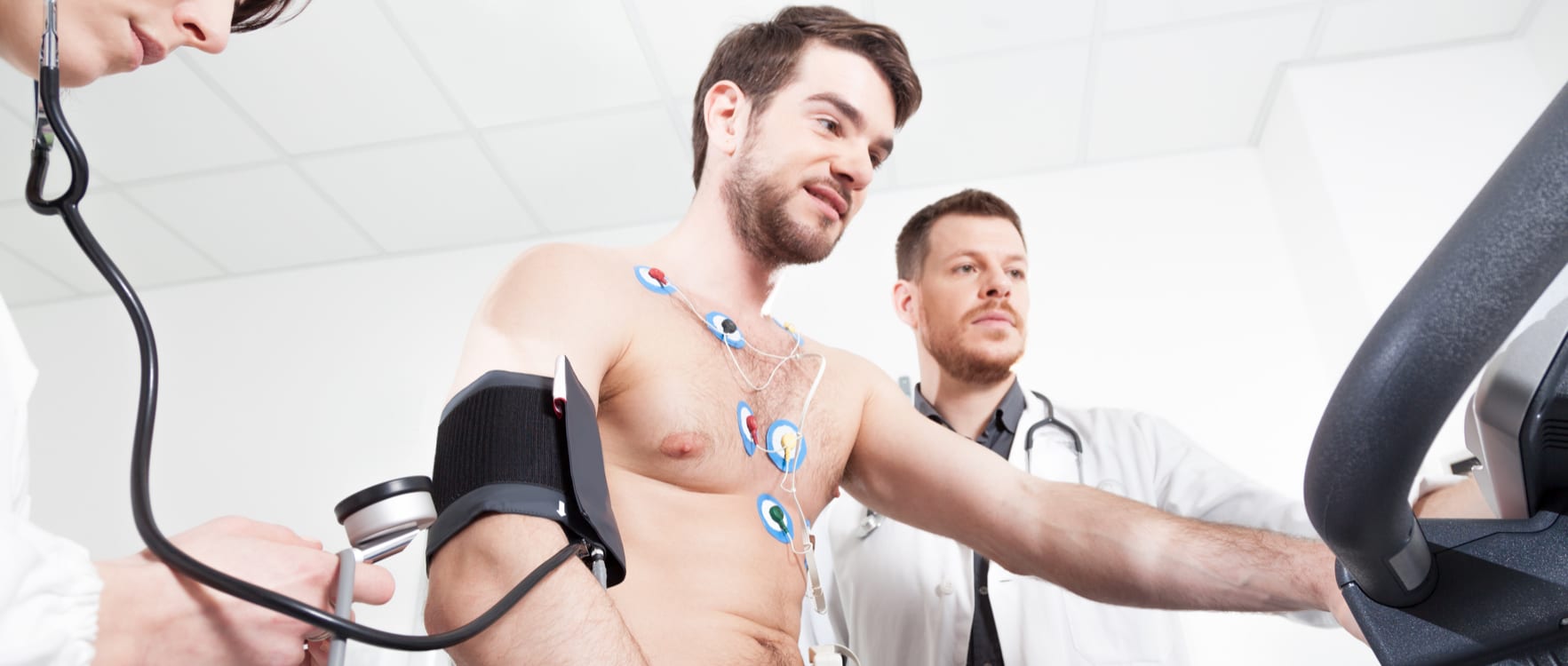 Two cardiologists measuring a patients heart rate with a treadmill, stethoscope and heart rate monitor