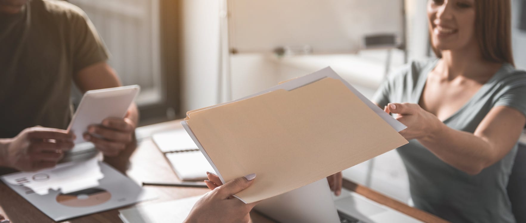 A woman handing a file with papers to another woman at an office table
