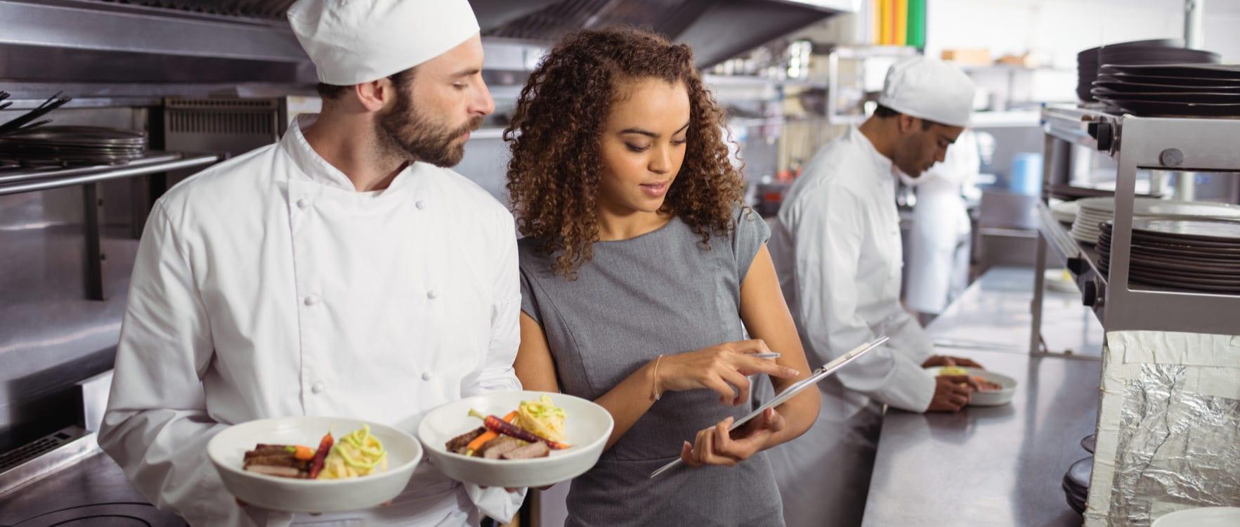 Caterer woman showing the cooking program to a chef in a kitchen