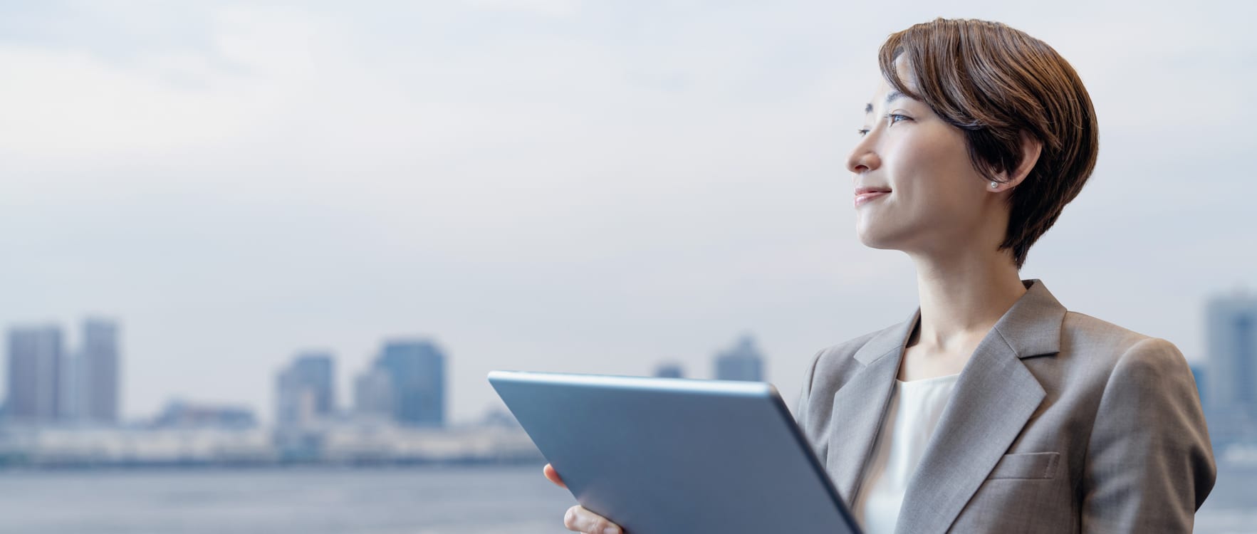 Businesswoman holding a tablet and looking forward with the city in the background