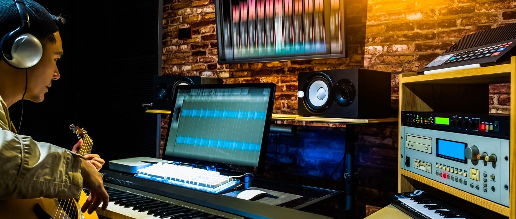 Male composer playing guitar with headphones in a recording studio