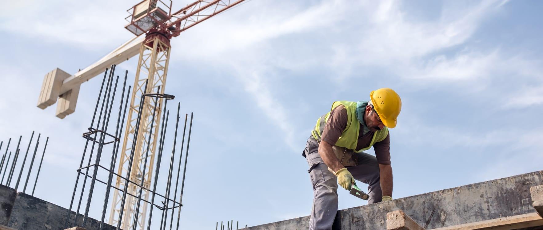 Construction worker hammering nails with a crane in the background