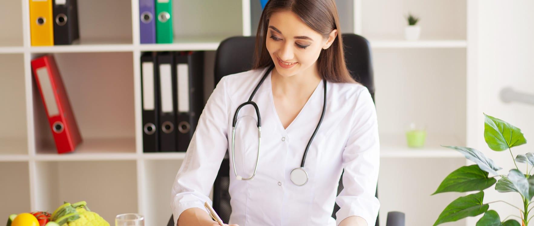 Woman dietitian with a stethoscope around her neck writing on her desk