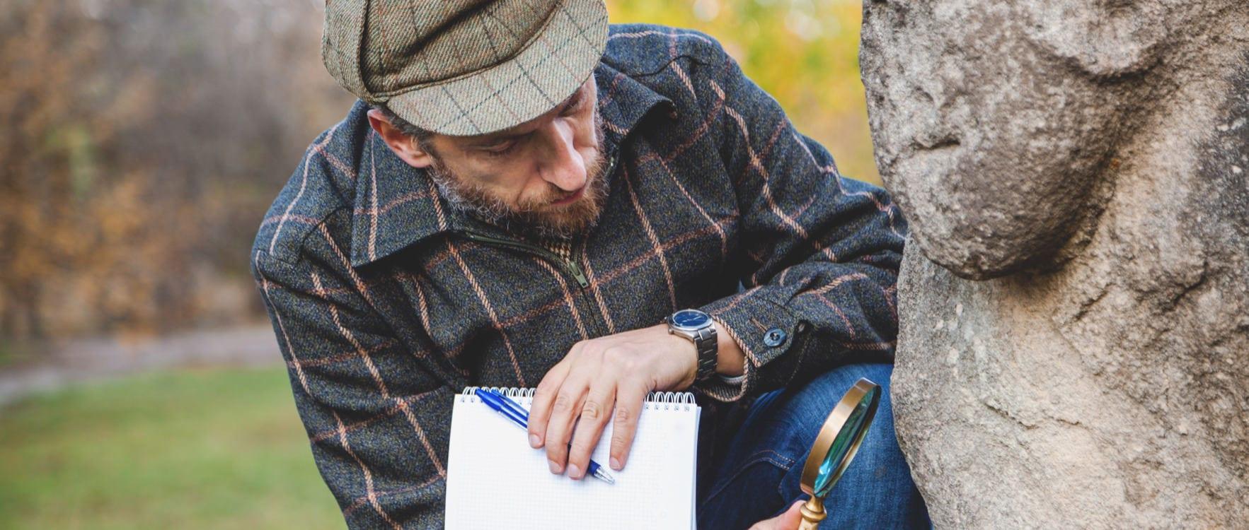 Man holding a note book while looking at a tree bark through a magnifiying glass