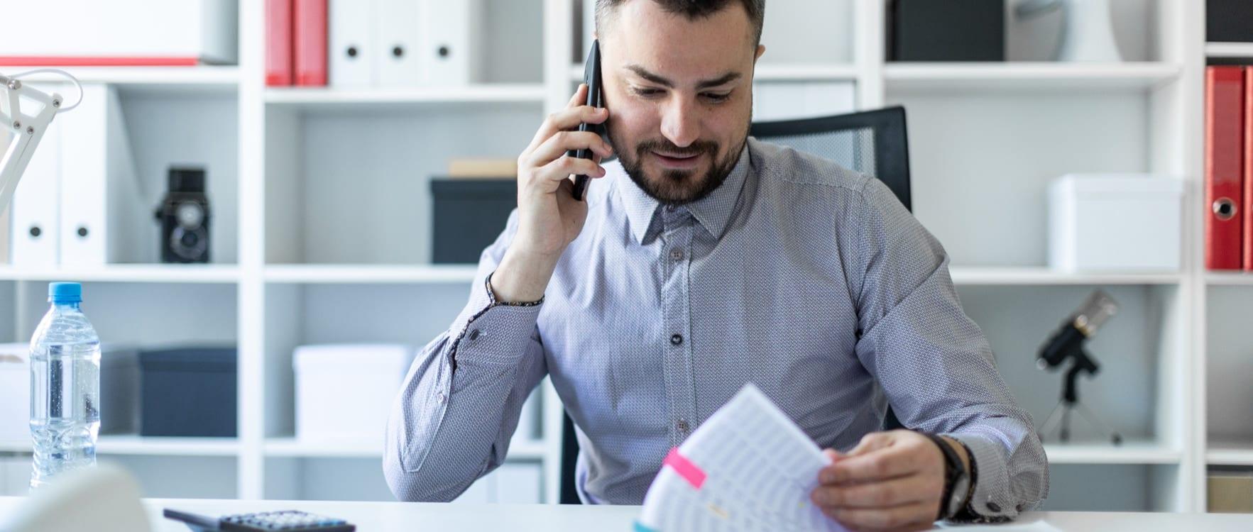 Businessman talking on the phone while viewing papers at his desk