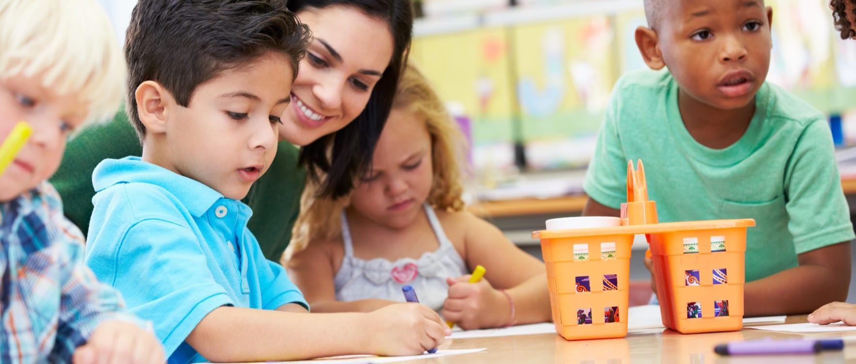 Woman teacher with a group of kindergarten children painting with crayons