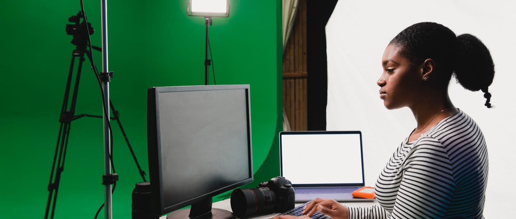 Woman using a computer at a photo studio with a green screen and lamps
