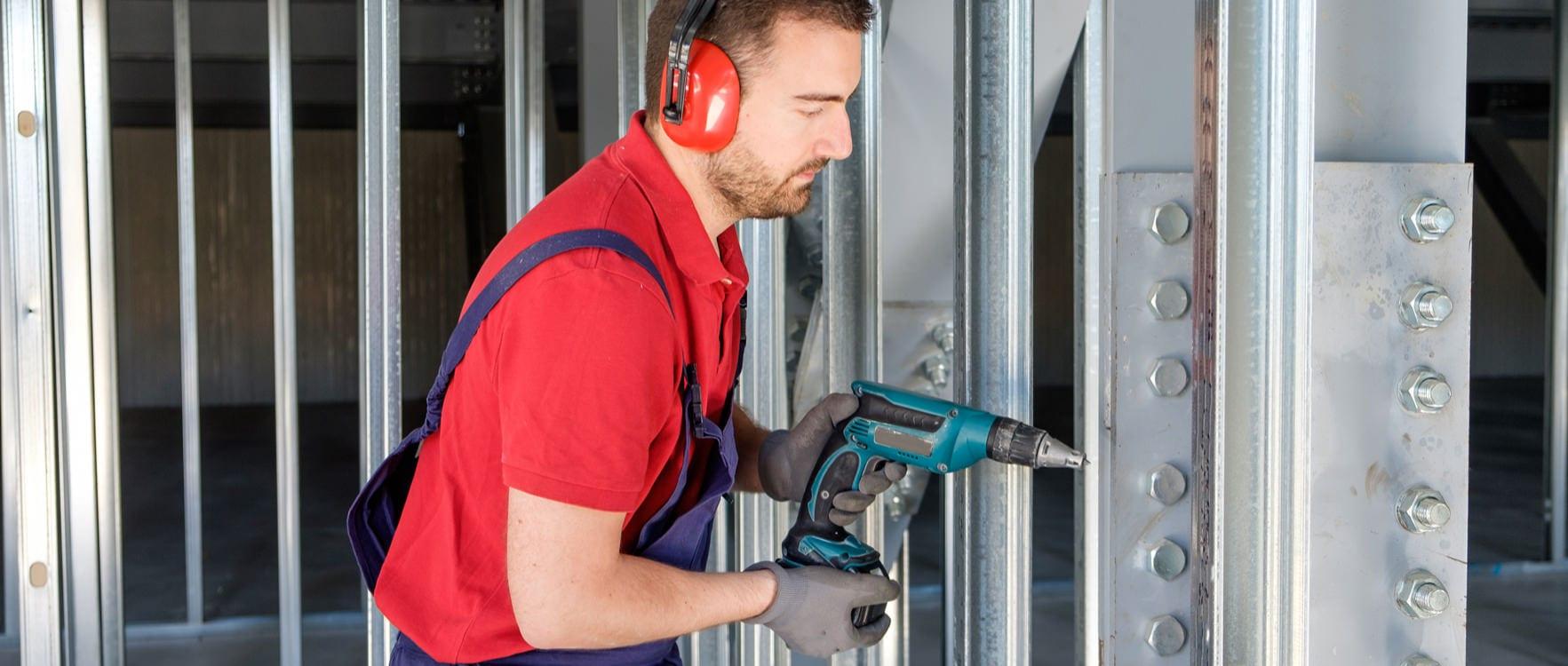 Man in working uniform using a drill at a construction site