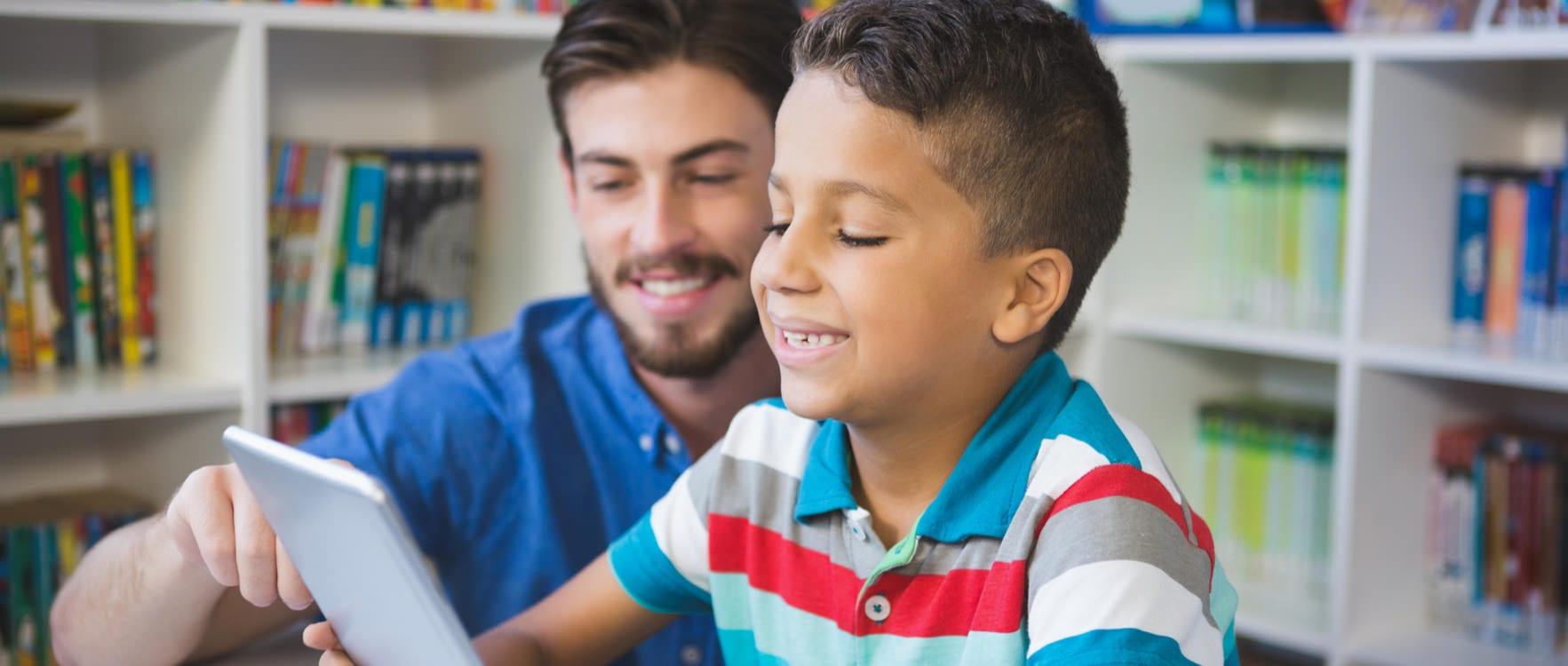 Male therapist helping a boy read from a tablet