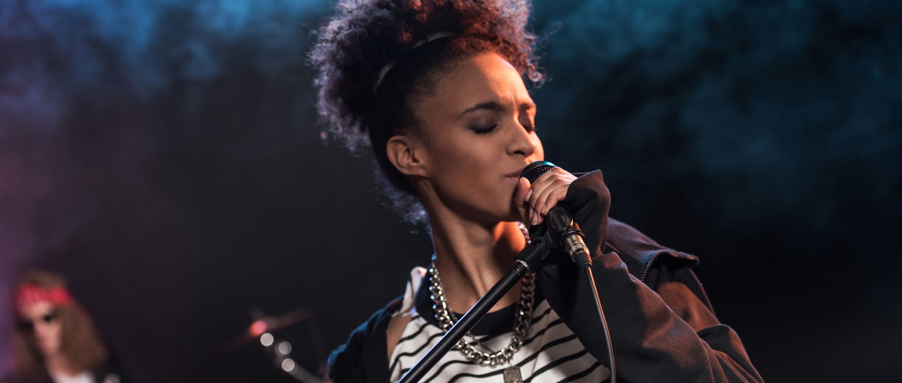 A woman singing to a microphone with a drummer in the background