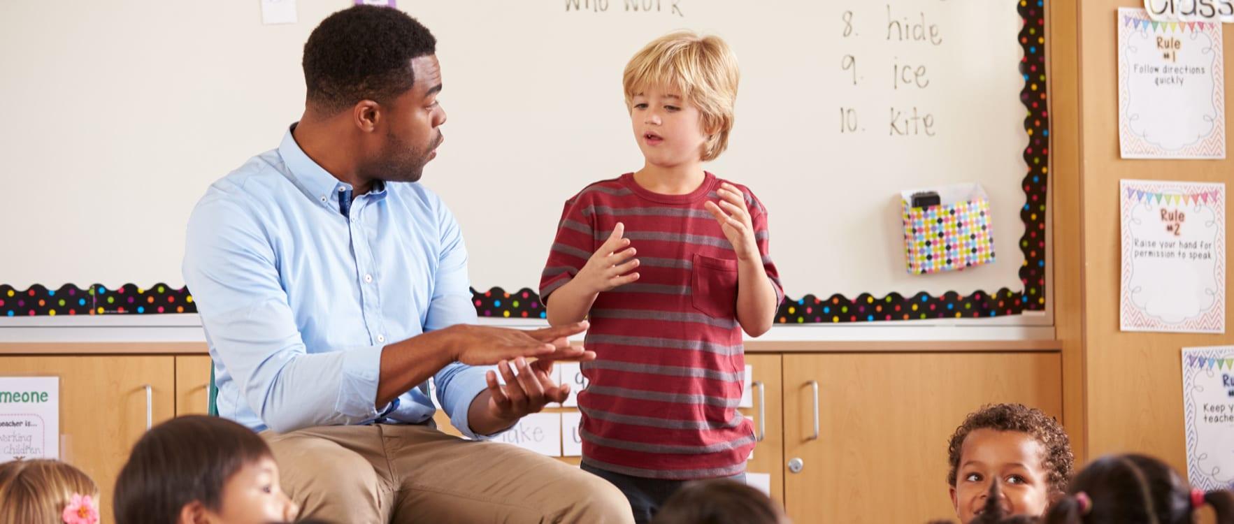 A male teacher in front of a class helping a boy in an oral presentation