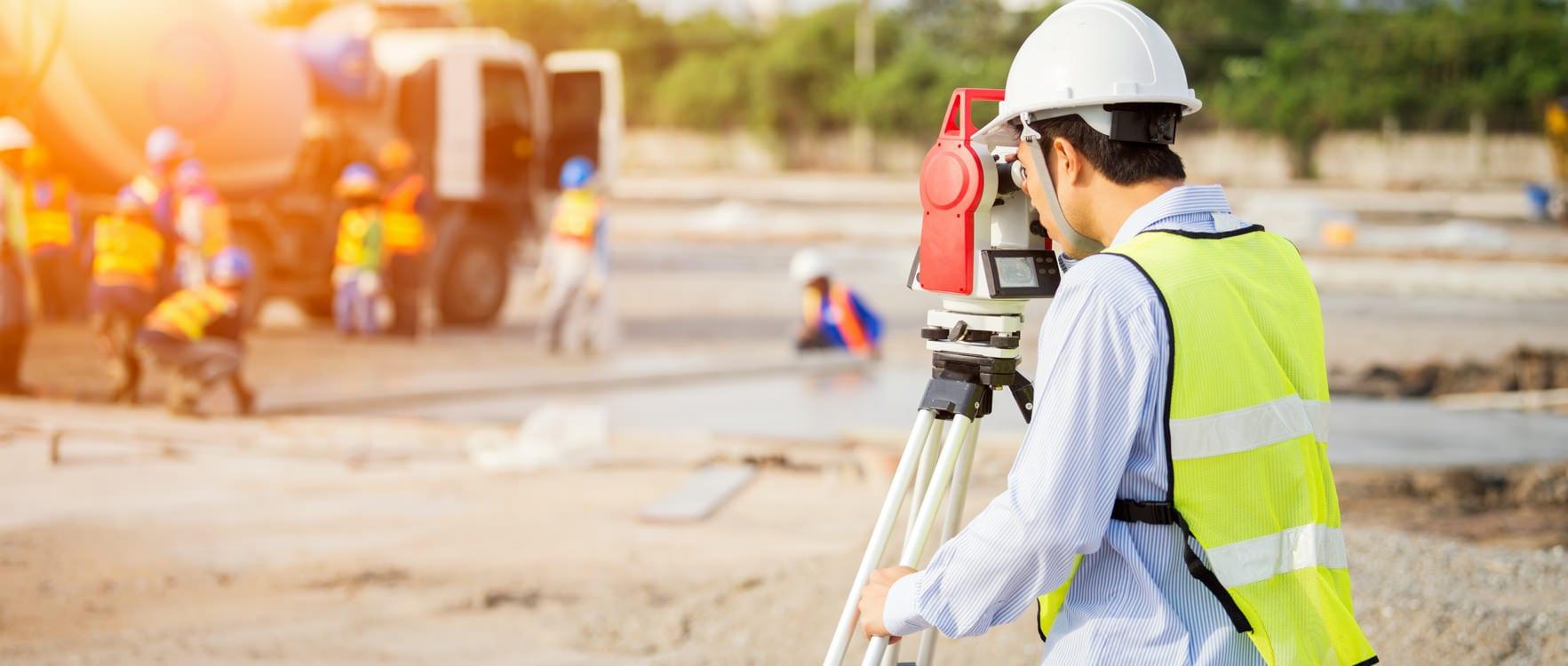 A man wearing a hard hat looking through a land surveyor