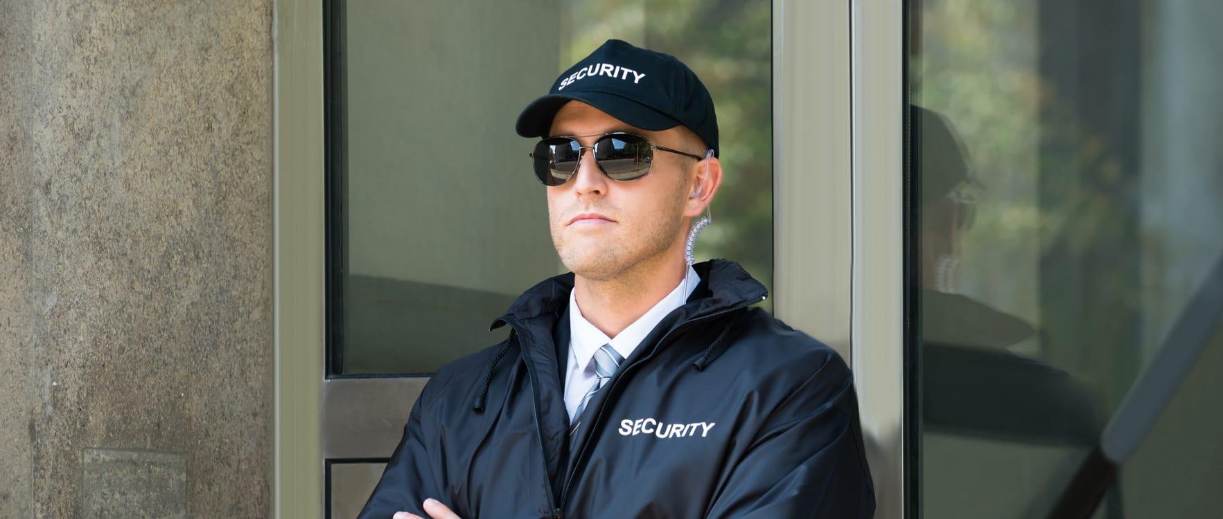 A security guard standing with his arms crossed in front of a door