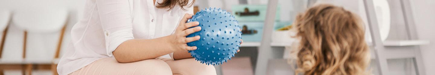 Woman holding a blue ball in front of a little girl