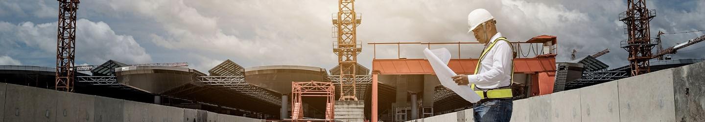 Engineer with a hard hat looking at blueprints at a construction site