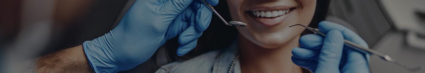 Dentist's hands holding dentist tools about to perform a check-up on a smiling patient