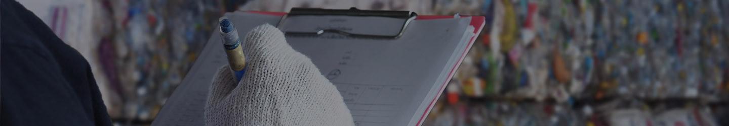 Hand with a glove tacking notes in a note pad at a garbage disposal facility